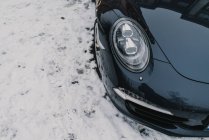 Von oben Aufnahme eines modernen schwarzen Autos, das auf frischem weißen Schnee auf der Stadtstraße steht — Stockfoto