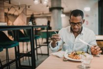 Adulto afro-americano homem desfrutando de deliciosa comida enquanto sentado à mesa em restaurante elegante — Fotografia de Stock