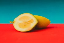 Дві половинки соковитого стиглого лимона на яскраво-червоній поверхні на синьому фоні — стокове фото