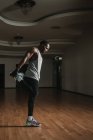 Vue latérale d'attrayant mec noir faire de l'exercice de réchauffement pour les jambes tout en se tenant dans la salle spacieuse de la salle de gym moderne — Photo de stock