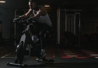 Homem negro sério em bicicleta de exercício no ginásio — Fotografia de Stock