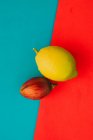 Fresh whole tamarillo and ripe lemon on bright red and blue background — Stock Photo