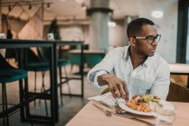 Hombre afroamericano adulto disfrutando de una deliciosa comida mientras está sentado en la mesa en un restaurante elegante - foto de stock