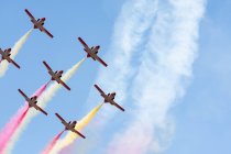 Grupo de chorros que emiten humo de color mientras vuelan sobre el fondo del cielo azul claro - foto de stock