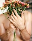 Jovem sem camisa cara segurando flores no fundo cinza — Fotografia de Stock
