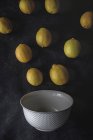 Fresh lemons on dark background with white bowl — Stock Photo