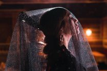 Vista lateral da mulher atraente em véu e vestido na cena iluminada por luzes — Fotografia de Stock