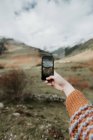 Crop mano della signora con telefono cellulare tiro pittoresco vista sulla valle con meravigliose montagne e cielo nuvoloso in Pirenei — Foto stock