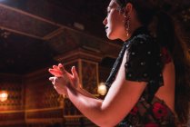 Vista laterale della giovane donna in abito battendo le mani e ballando sulla scena vicino a sedie in camera di lusso decorata da mosaico — Foto stock