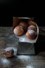 Fresh cake near set of baked loaf in craft paper with powdered sugar on wooden table in darkness on black background — Stock Photo
