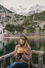 Jovem senhora sentada no banco de olhos fechados perto de uma vista incrível da superfície da água entre altas montanhas com árvores na neve em Pirinéus — Fotografia de Stock