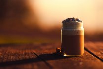 Aromatische Zimtstangen neben Glas leckeren Kaffees mit Sahne auf Holztisch — Stockfoto