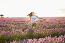 Happy attractive lady spinning between beautiful purple flowers on lavender field — Stock Photo
