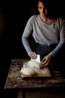 Crop pâte humaine tenant avec de la farine sur planche à découper près de la table en bois sur fond noir — Photo de stock
