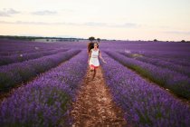 Молода жінка в сукні біжить між фіолетовим лавандовим полем — стокове фото