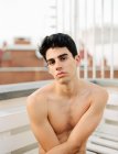 Jovem sem camisa cara olhando para a câmera e sentado na varanda no fundo borrado — Fotografia de Stock