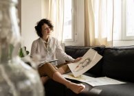 Жінка малює на папері на дивані в кімнаті — стокове фото