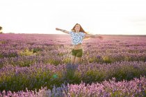 Young woman spinning with arms outstretched between violet lavender field — Stock Photo