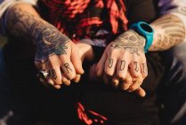 Обрезанный образ мужчины в татуировках с кольцом и часами держась за руки женщины с красным шарфом в солнечную погоду — стоковое фото