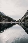 Amazing view of water surface between high mountains with trees in snow and cloudy heaven in Pyrenees — Stock Photo