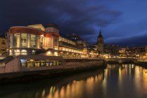 Uferpromenade der modernen Stadt mit hellen Lichtern alter Gebäude unter dunklem Dämmerhimmel, die sich im Flusswasser spiegeln — Stockfoto