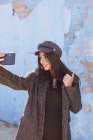 Sorrindo senhora hispânica tomando selfie perto de parede azul gasto — Fotografia de Stock