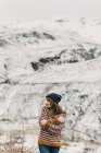 Atractiva joven en suéter y sombrero con las manos cruzadas cerca de la colina sobre fondo borroso en los Pirineos - foto de stock
