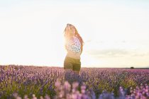 Femme debout entre grand champ de lavande violette au coucher du soleil — Photo de stock