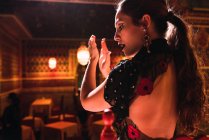 Вид збоку на молоду жінку в сукні, що плескає руками і танцює на сцені біля стільців в розкішній кімнаті, прикрашеної мозаїкою — стокове фото