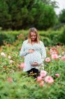 Улыбающаяся беременная привлекательная женщина между цветами — стоковое фото