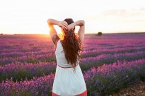 Woman standing between big violet lavender field at sunset — Stock Photo