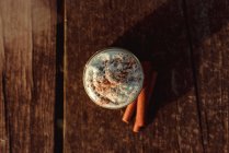Bâtonnets de cannelle aromatiques près du pot de café délicieux avec de la crème sur la table de bois — Photo de stock