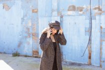 Hispanic stylish young woman talking on smartphone while walking on street in front of shabby wall — Stock Photo