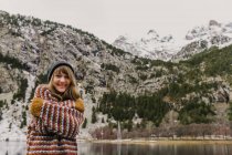 Attraktive junge Frau in Pullover und Hut mit verschränkten Händen in der Nähe eines Hügels vor verschwommenem Hintergrund in den Pyrenäen — Stockfoto