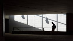 Silhouette eines jungen Mannes mit Rucksack, der in der Nähe von Treppenhaus in modernem Gebäude steht — Stockfoto