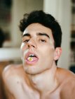 Young shirtless guy with fresh flower in opened mouth looking at camera on blurred background — Stock Photo
