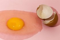 Raw egg yolk and eggshell on pink background — Stock Photo