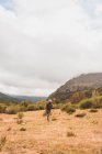 Vista lateral da senhora de chapéu e casaco de esqui com mochila e bengala andando no prado perto da montanha em nuvens em Isoba, Castela e Leão, Espanha — Fotografia de Stock