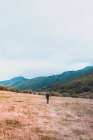 Vista lateral de humano com mochila no prado, céu nublado e vista sobre montanhas com floresta em Isoba, Castela e Leão, Espanha — Fotografia de Stock