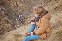 Mignon garçon assis sur la colline près du ruisseau — Photo de stock