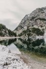 Удивительный вид на водную поверхность между высокими горами с деревьями в снегу и облачным небом в Пиренеях — стоковое фото
