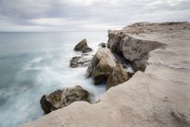 Ruvida scogliera di pietra e ondeggiante mare tempestoso sotto cielo nuvoloso — Foto stock