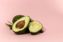 Свежие целые и наполовину авокадо на розовом фоне — стоковое фото