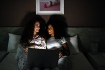 Young cheerful friends in bed entertained on their computer watching movies by night — Stock Photo