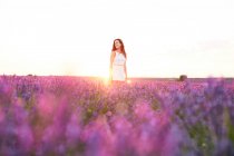 Усміхнена молода жінка між фіолетовим лавандовим полем під підсвічуванням — стокове фото