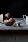 Pastel fresco cerca del juego de pan horneado en papel artesanal con azúcar en polvo en la mesa de madera en la oscuridad sobre fondo negro - foto de stock