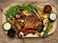 Миски з різними соусами розташовані поруч зі смаженим м'ясом та овочами, знятими зверху — стокове фото