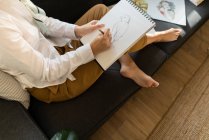 Женщина рисует на бумаге на диване в комнате — стоковое фото