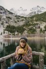 Jovem senhora sentada no banco de olhos fechados perto de uma vista incrível da superfície da água entre altas montanhas com árvores na neve em Pirinéus — Fotografia de Stock