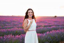 Smiling young woman in dress showing flowers between violet lavender field — Stock Photo